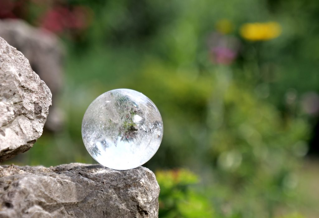 Durchsichtige Glaskugel auf einem Naturstein im Garten, Symbolbild für Klarheit und innere Ruhe